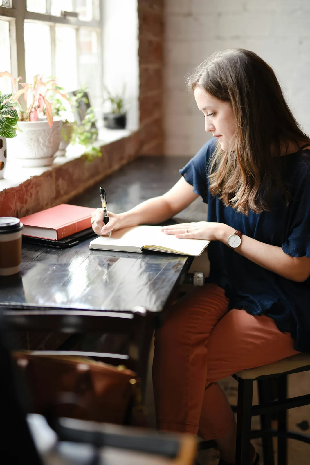 An author writing in a notebook at a desk by the window