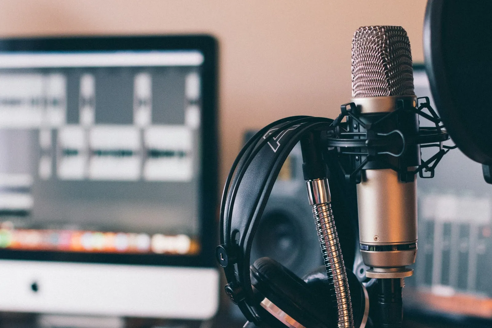 Headphones hanging on a studio microphone beside a recording screen